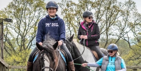 Two women riding horses with Sport In Mind charity t-shirts on